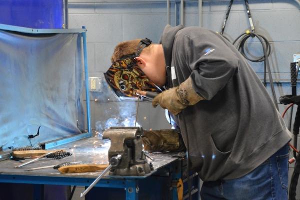 high school student wearing protective equipment and welding
